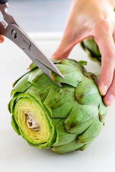 a person cutting an artichoke with a pair of scissors on top of it