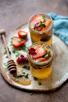 two glasses filled with liquid sitting on top of a plate next to honey and strawberries