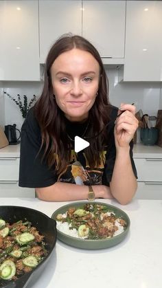 a woman sitting at a table with two pans of food in front of her