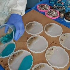 a person in blue gloves pours some liquid into small pie crusts on a table