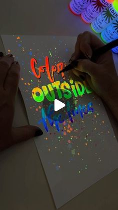 someone is drawing on paper with colored ink and watercolors in front of them