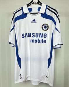 a white and blue soccer jersey hanging on a wall next to a hanger with the words samsung mobile written on it