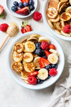 two bowls filled with bananas, strawberries and other fruit on top of a white table