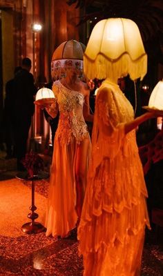 two mannequins dressed in orange dresses stand next to each other with lamps on either side