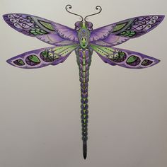 a purple and green dragonfly sitting on top of a white wall