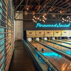 bowling lanes lined up against the wall with neon signs above them that read pinewood social