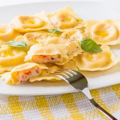 a white plate topped with ravioli covered in cheese sauce and garnished with basil