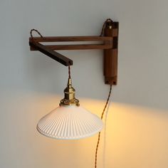 a wall light hanging from the side of a white wall next to a wooden shelf