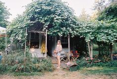 a woman sitting on a chair in front of a house surrounded by trees and bushes