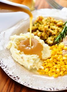 a plate with mashed potatoes, corn and gravy being drizzled over