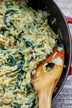 a pot filled with pasta and spinach on top of a table next to a wooden spoon