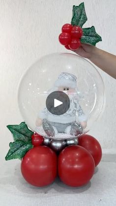 a snow globe with santa clause on top and red balls in the bottom, surrounded by holly leaves