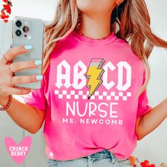 a woman wearing a pink shirt and holding a cell phone in her hand with the words abcd nurse on it