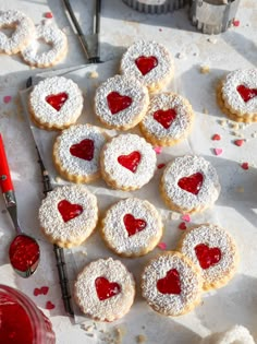 heart - shaped sugar cookies with powdered sugar and jelly on the table next to them