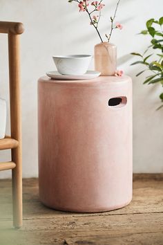 a pink stool with a cup and saucer on it next to a potted plant