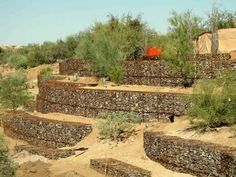 a stone wall in the middle of a desert area with trees and bushes around it