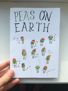 a hand holding up a piece of paper that says peas on earth