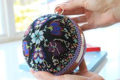 a hand holding a small beaded purse on top of a table next to a window