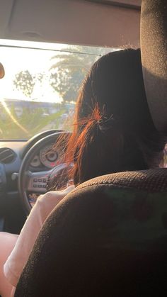 the back end of a woman's head as she sits in a car with her hands on the steering wheel