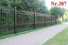 an iron fence on the side of a brick walkway next to a sidewalk with grass and trees