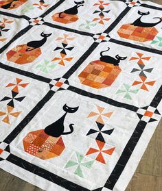 a black cat sitting on top of an orange and green patchwork table runner quilt