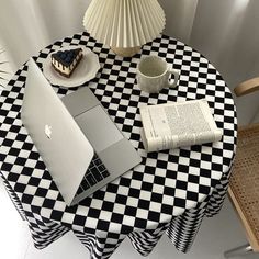 an open laptop computer sitting on top of a checkered table cloth next to a cup and saucer