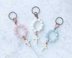 three key chains with cross charms on them sitting on a marble counter top next to each other