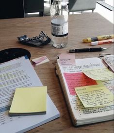 an open notebook with sticky notes on it next to a bottle of water and other office supplies