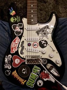 an electric guitar with stickers on it sitting in someone's lap and looking at the camera