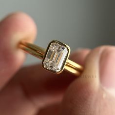 a close up of a person's hand holding a gold ring with an emerald stone