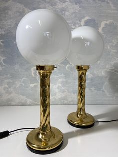 two white and gold lamps sitting on top of a table next to a black cord