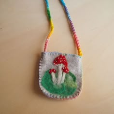 a small felt bag with a mushroom on the front and a rainbow thread cord attached to it