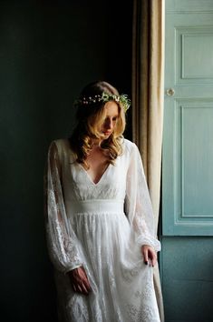 a woman wearing a white dress standing next to a window with her hands on her hips