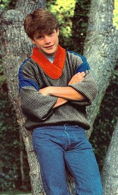 a young man leaning on a tree with his arms crossed