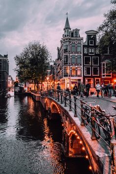 people are walking along the side of a river at night with buildings in the background