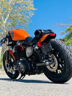 an orange and black motorcycle parked on the side of the road with trees in the background