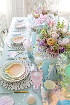 the table is set with plates, cups and vases for an ocean themed party