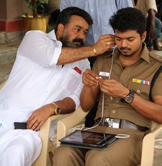 two men are sitting in chairs and one is using an electronic device