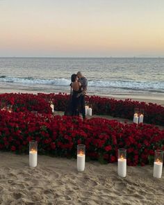 two people standing in front of flowers and candles on the beach with water behind them