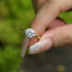 a woman's hand holding a diamond ring on top of her finger with grass in the background