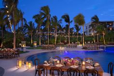 an outdoor dining area next to a pool at night with lit candles on the tables