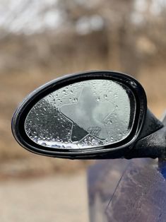 the side view mirror on a blue car is covered with water droplets and has an image of a person's face in it