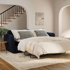 a bed sitting in the middle of a living room next to a stair case on top of a hard wood floor