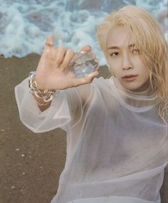 a woman with blonde hair is holding up a crystal ball in front of the ocean