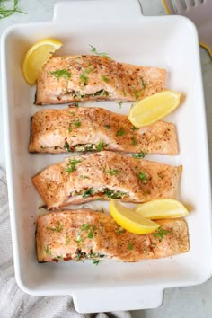 four salmon fillets in a white dish with lemon wedges