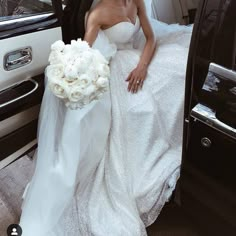 a woman in a wedding dress sitting on the back of a car