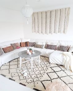 a living room filled with lots of white furniture and pillows on top of a rug