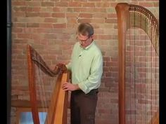 a man standing in front of a large wooden harp with his hands on the strings