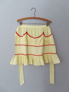 a yellow skirt with red trims hanging on a hanger