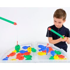 a young boy playing with an assortment of colorful plastic toy fish in a tray on a white background